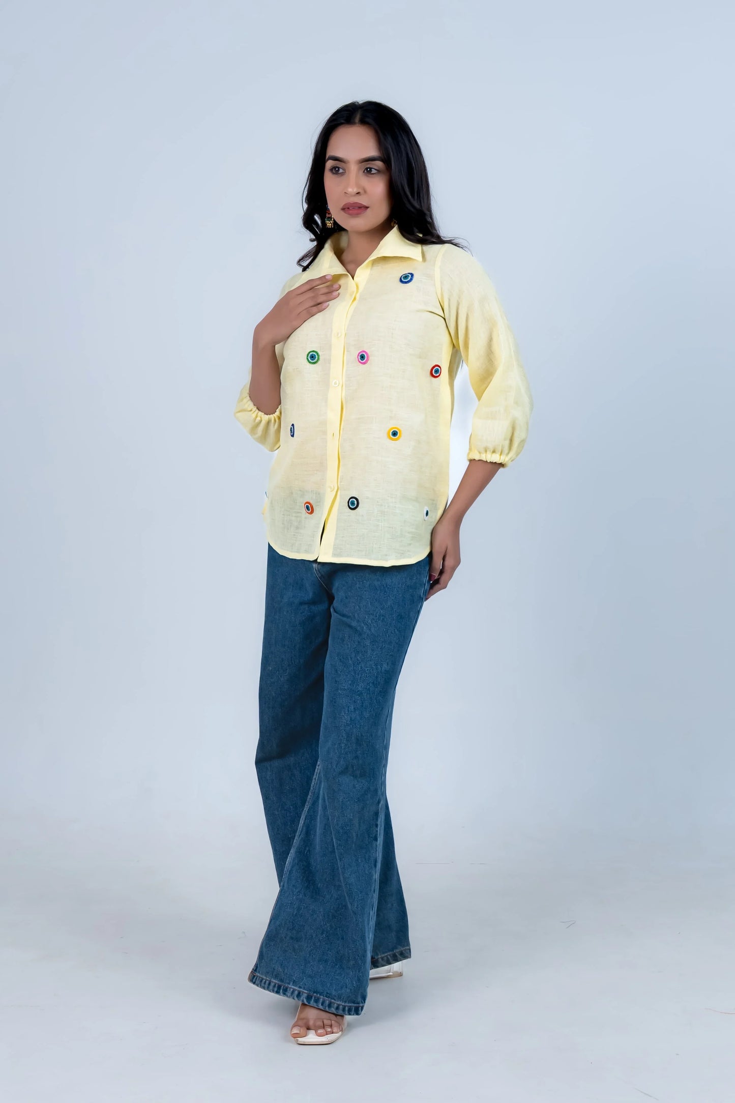 Yellow embroidered button-up shirt with colorful eye motifs, paired with blue flared jeans for casual wear