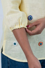 Yellow blouse with beaded eye buttons and ruffled sleeves, paired with denim.