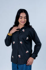 Woman wearing black shirt with popcorn embroidery, gold bangles, and blue jeans