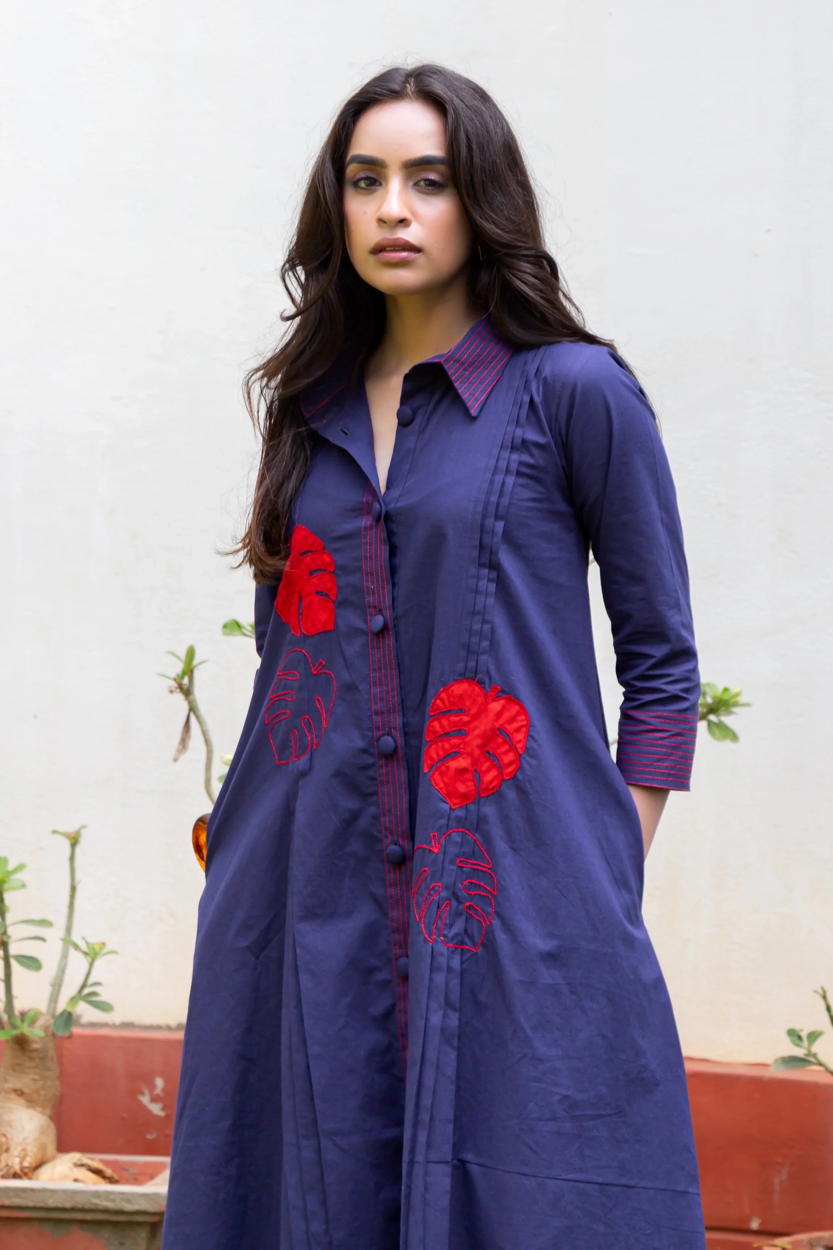 Woman wearing a navy blue embroidered dress with red leaf patterns and striped collar and cuffs, standing outdoors