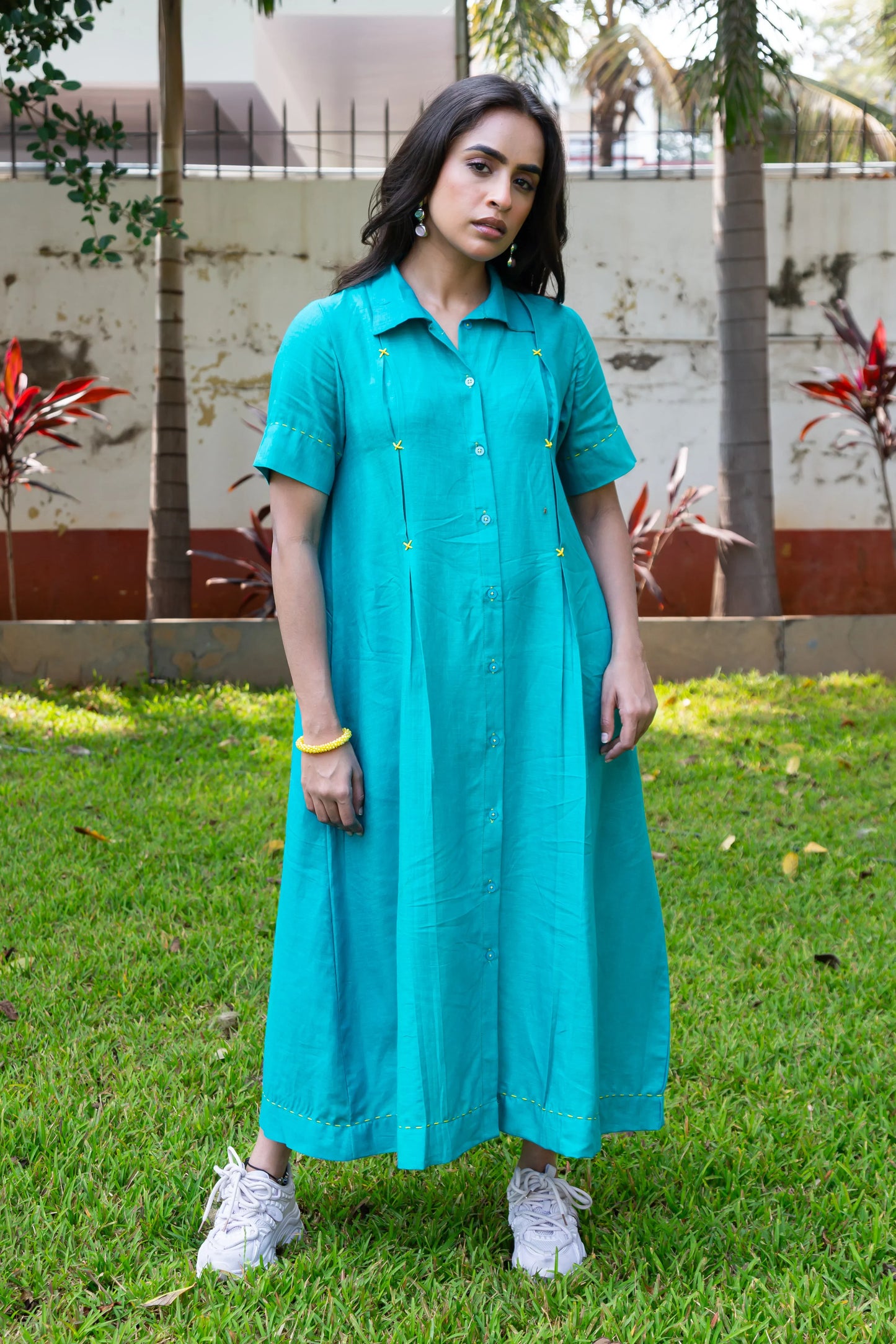Turquoise button-down dress with yellow stitching, paired with white sneakers, worn outdoors on grass.