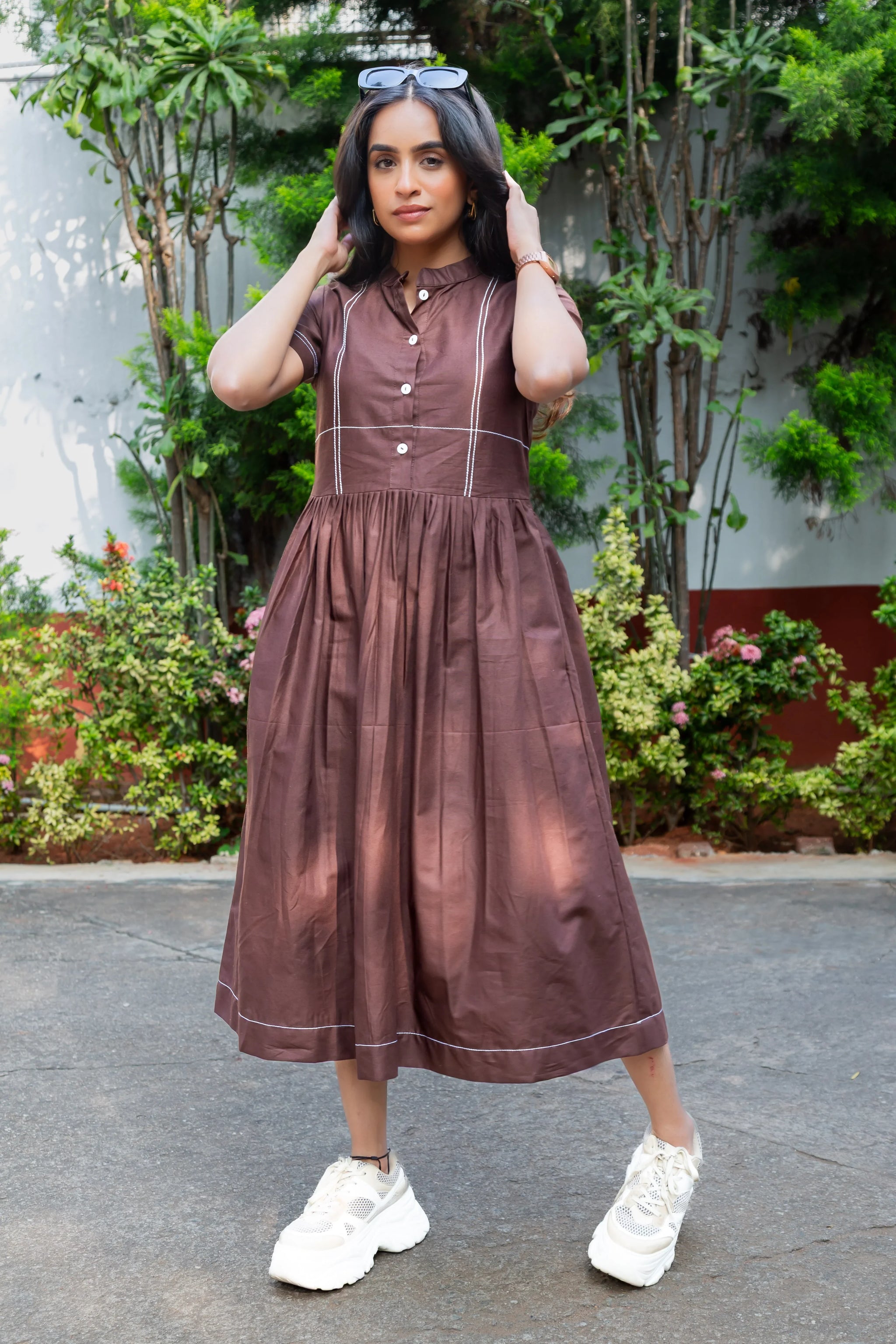 Brown button-front midi dress with white stitching, paired with white sneakers, styled outdoors