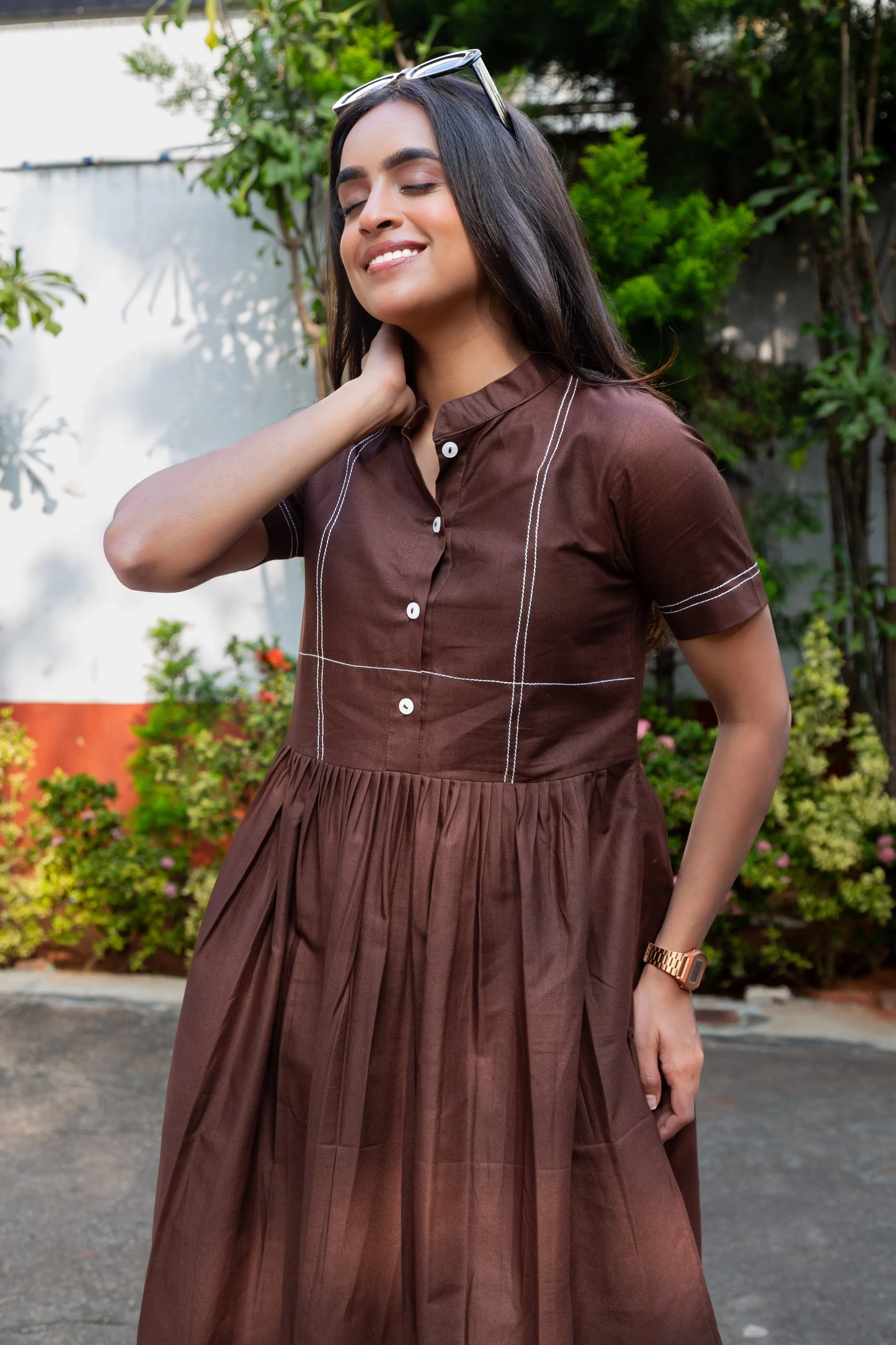 Woman in brown button-front dress with white stitching, outdoor garden setting