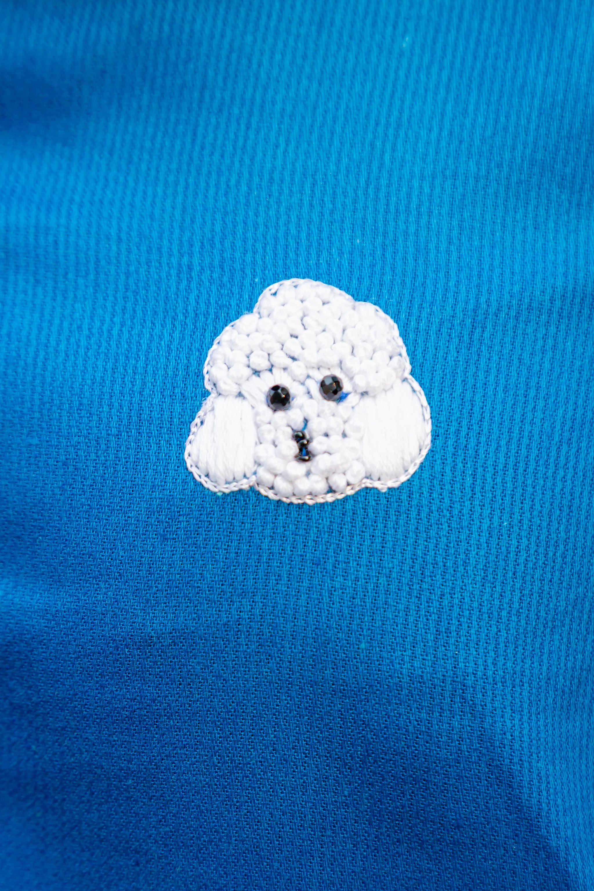 Cute white poodle embroidery on blue fabric, stylish women's apparel detail