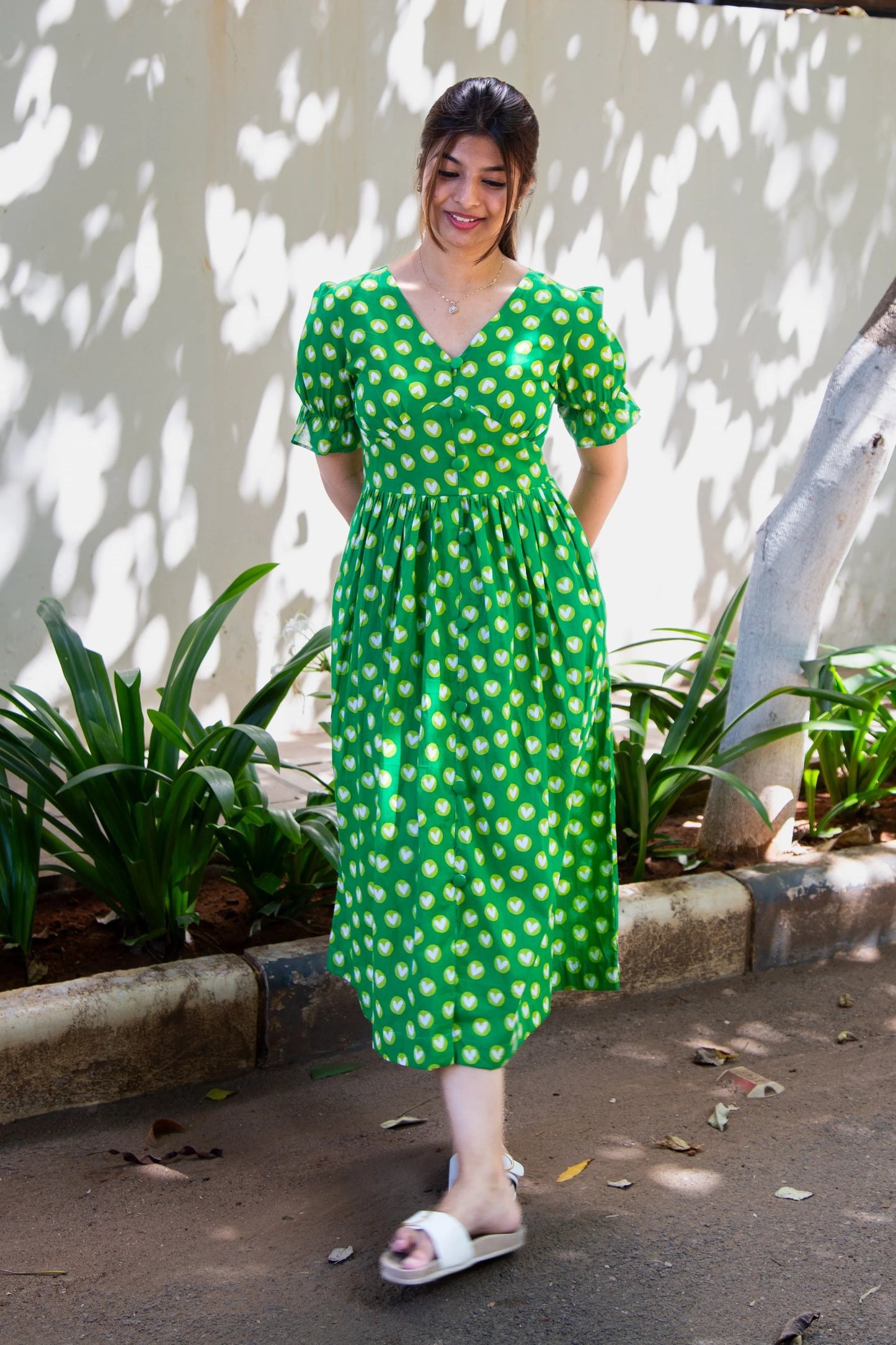 Green heart-print midi dress with puff sleeves, V-neck, and front buttons, styled with white sandals outdoors.