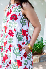 White sleeveless dress with red floral print and green leaves, worn with gold bangles