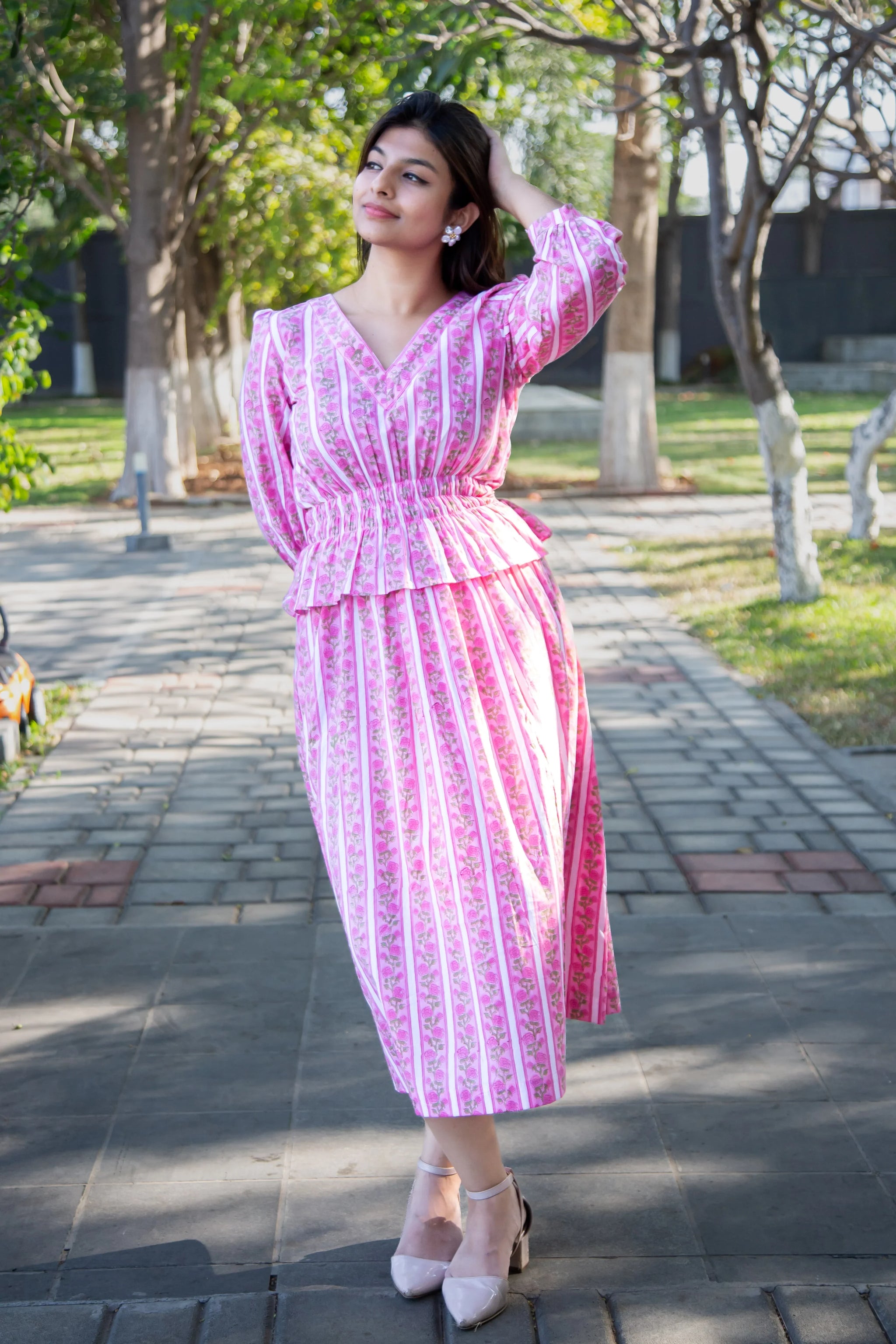 Woman in pink floral striped dress, posing outdoors on a sunny day