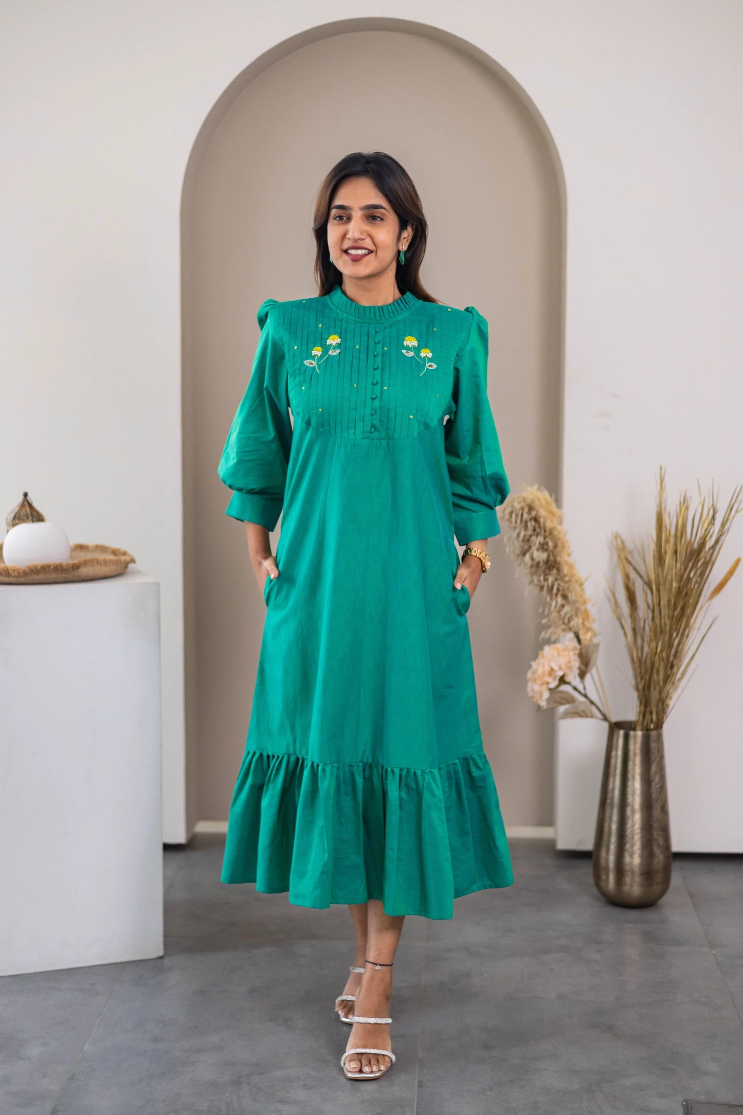 Woman wearing a green midi dress with floral embroidery, ruffle hem, and three-quarter sleeves