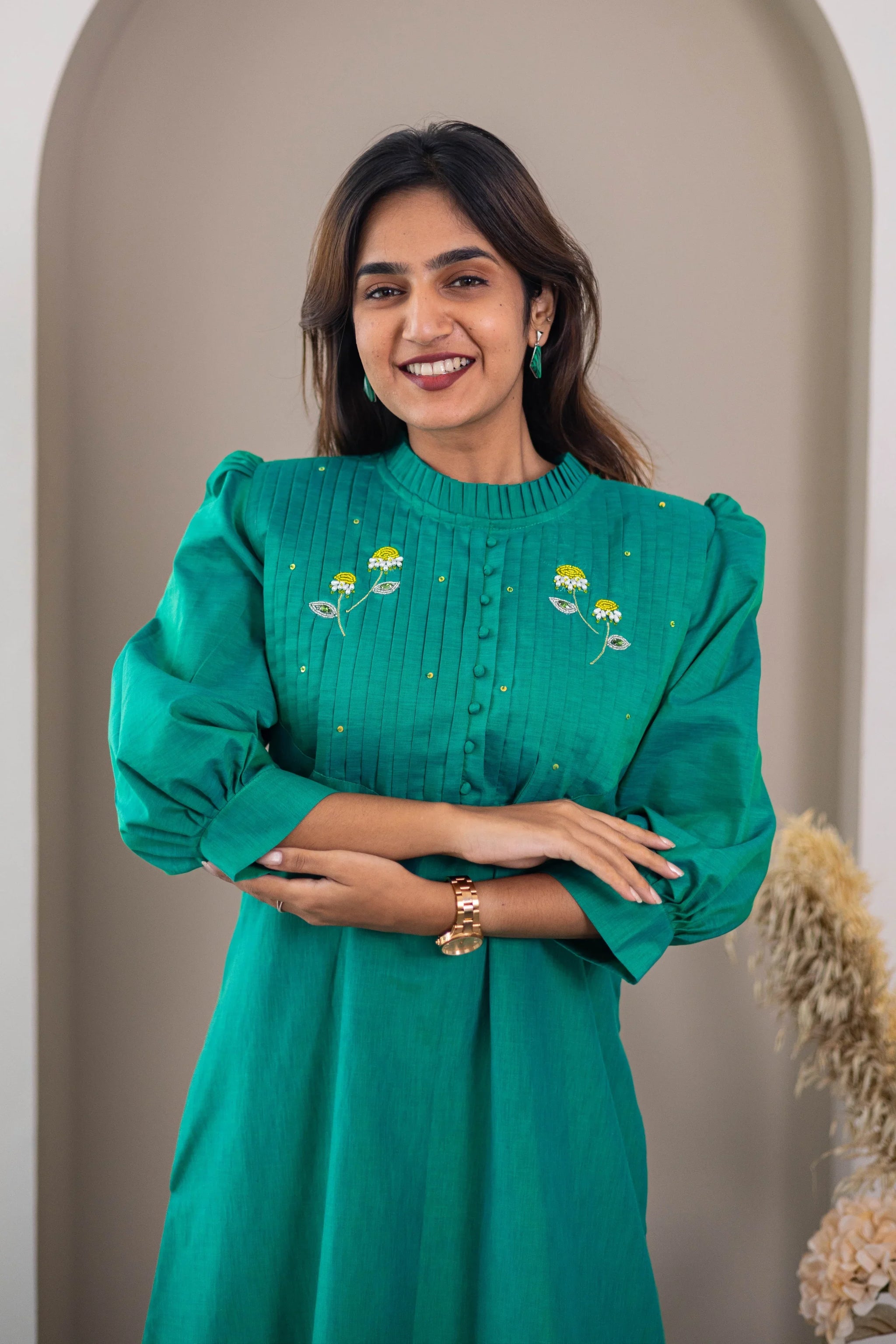 Woman wearing a green dress with floral embroidery and puff sleeves, smiling indoors