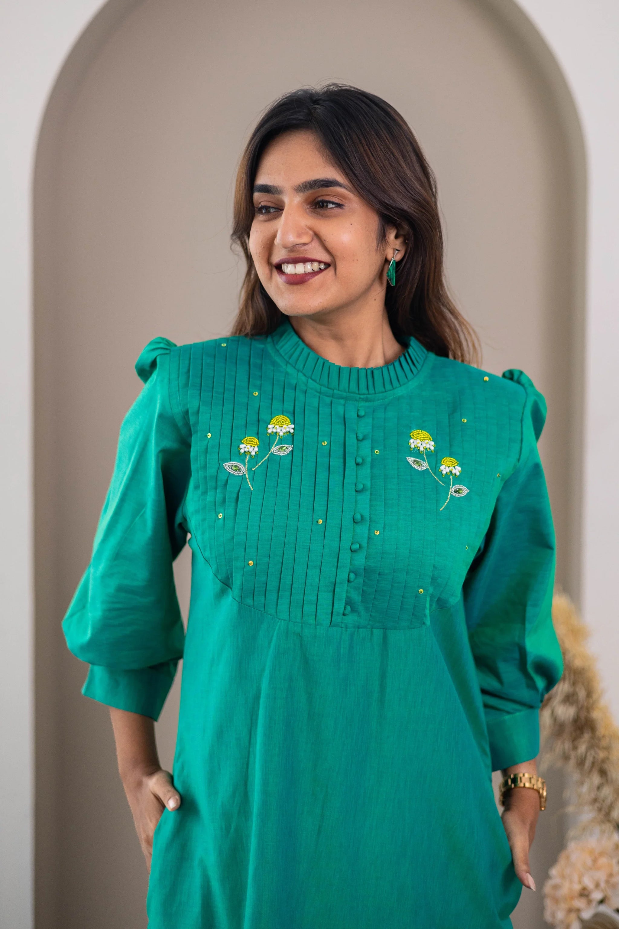 Woman wearing green dress with yellow floral embroidery and pintuck detailing