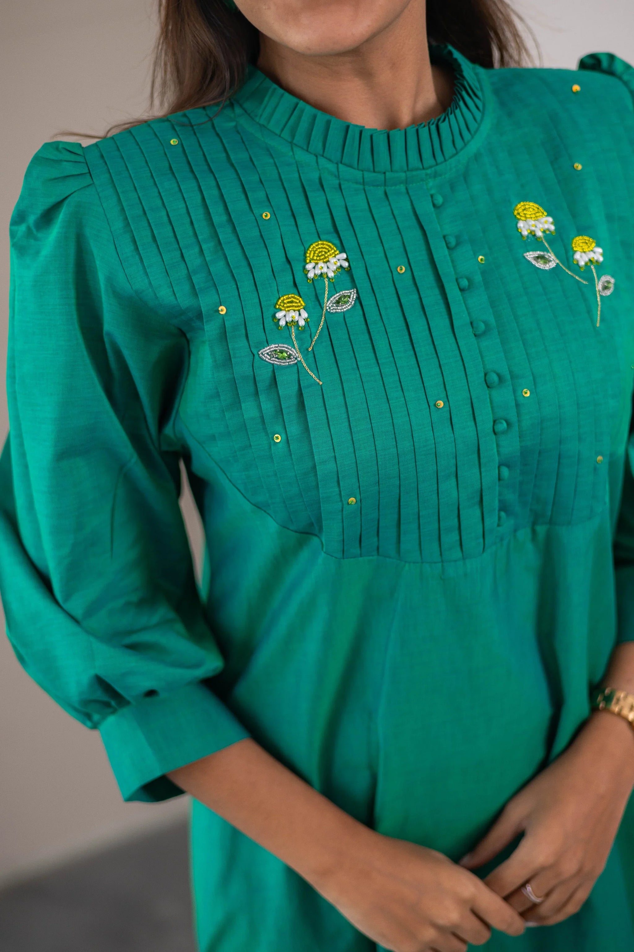 Green women’s dress with pleated front, yellow floral embroidery and gold studs