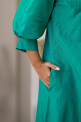 Close-up of woman wearing green dress with puff sleeve and hand in pocket