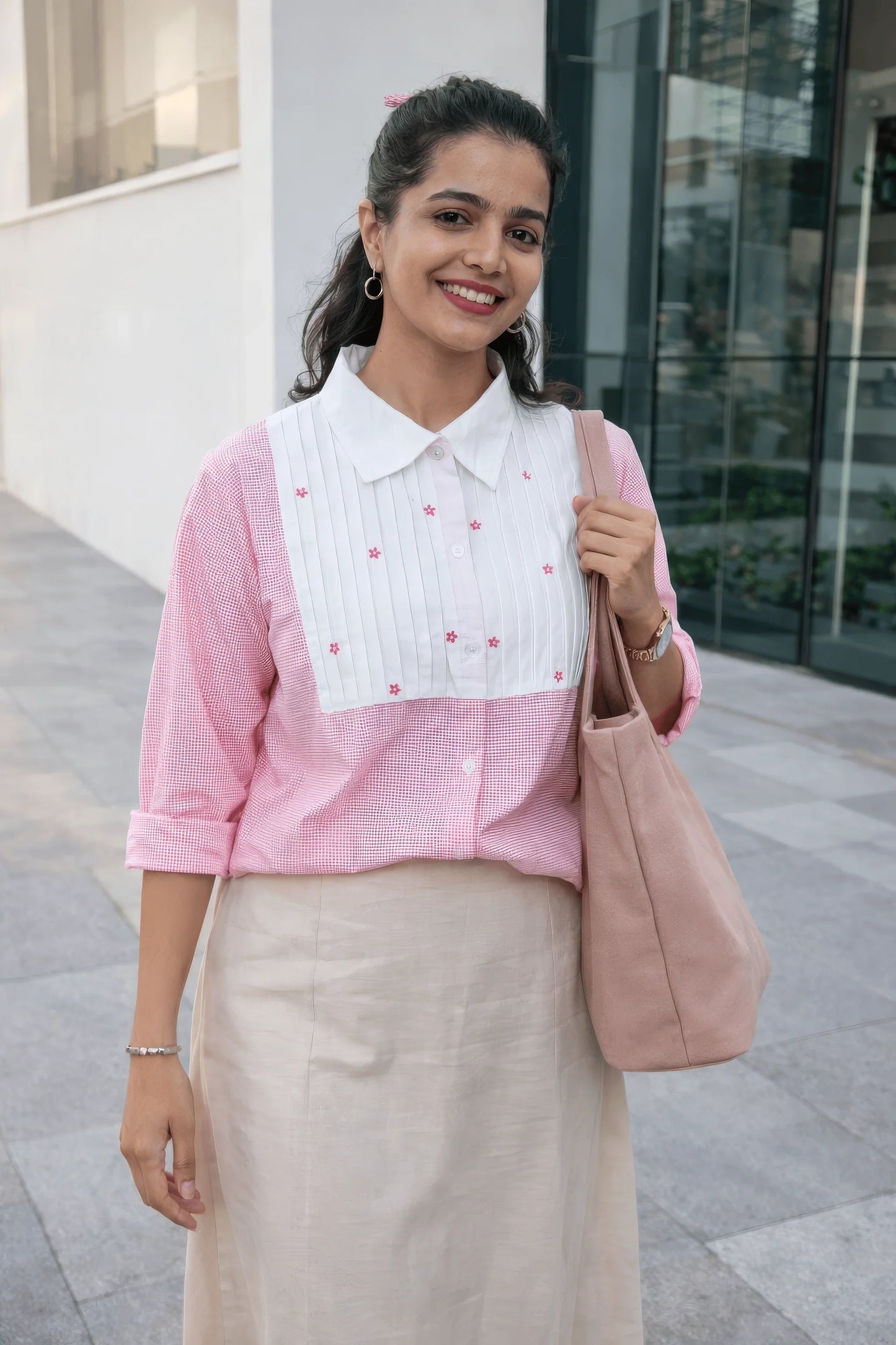 Woman in pink and white floral blouse with beige skirt, carrying pink tote bag, stylish everyday outfit