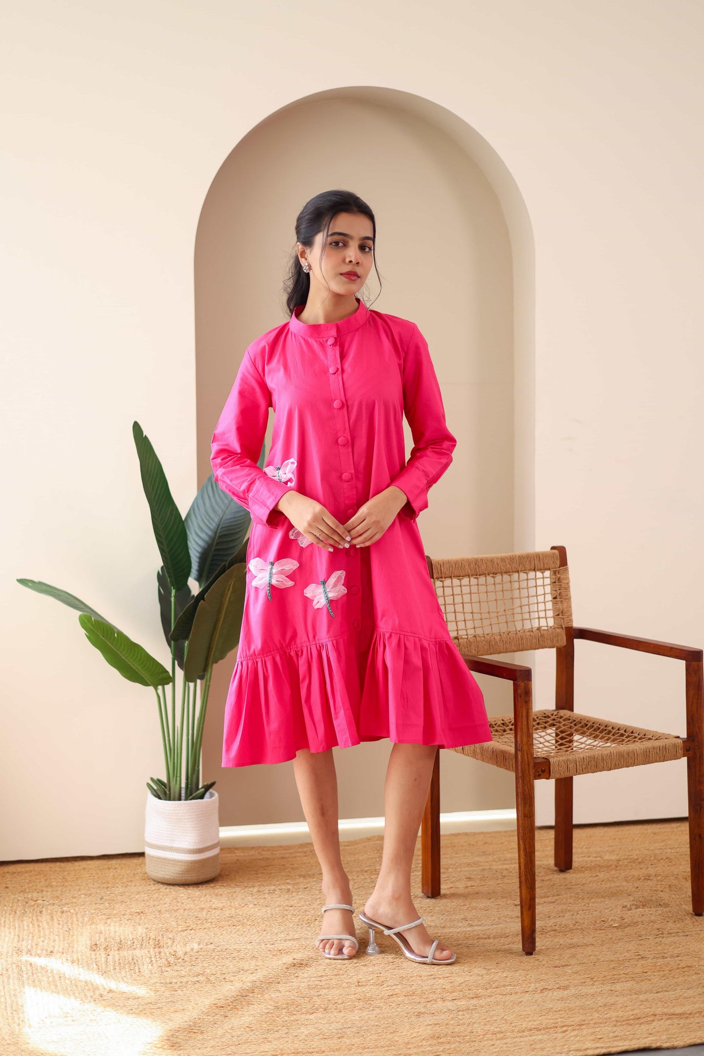 Woman wearing pink cotton dress with dragonfly embroidery, long sleeves, and ruffle hem
