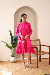 Woman wearing pink cotton dress with dragonfly embroidery, long sleeves, and ruffle hem
