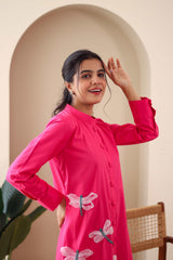 Woman wearing a pink cotton dress with dragonfly embroidery, long sleeves, front buttons