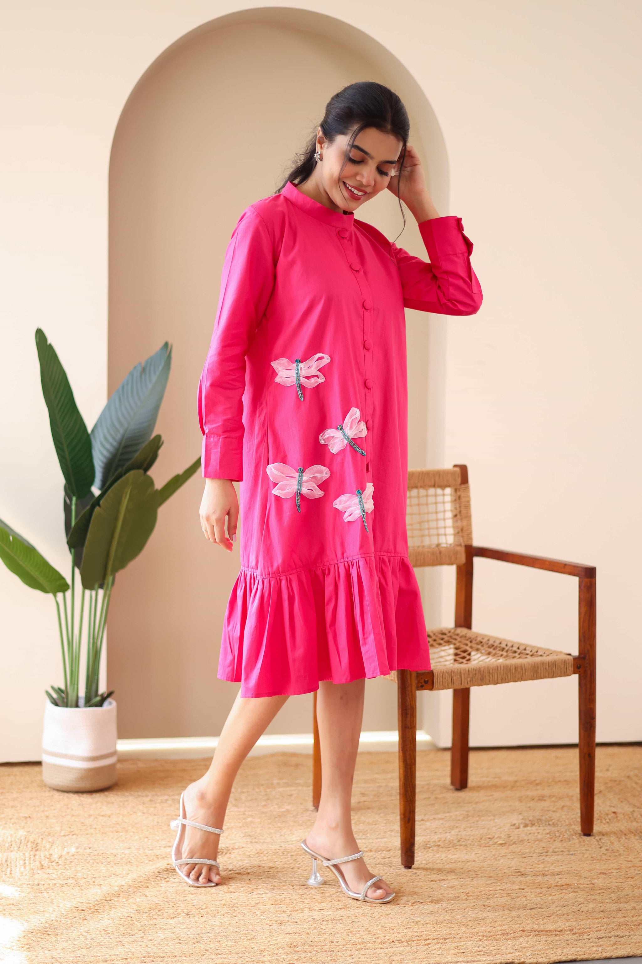 Woman wearing pink cotton dress with dragonfly embroidery and ruffle hem