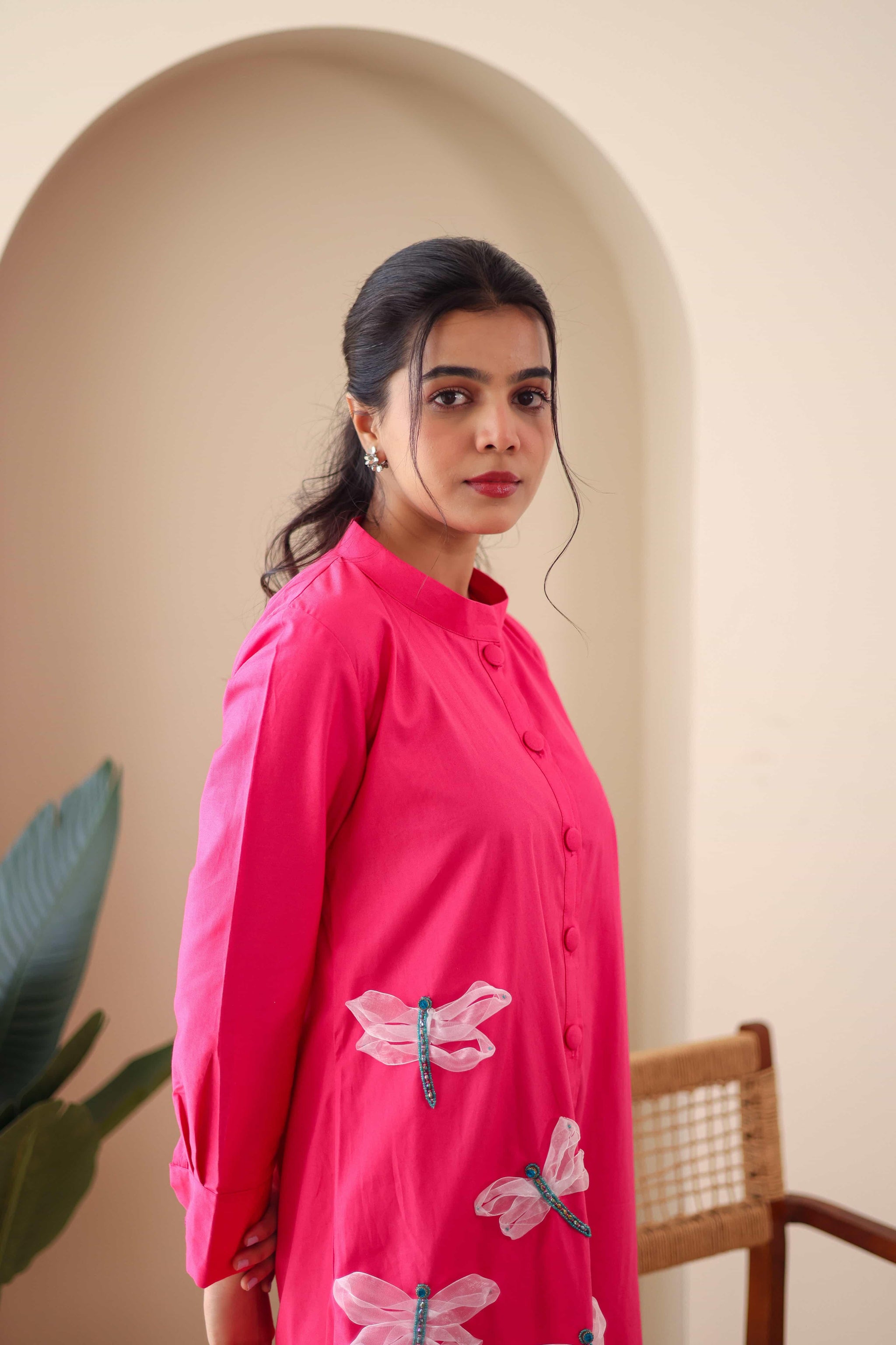 Woman wearing pink cotton dress with dragonfly embroidery, standing indoors