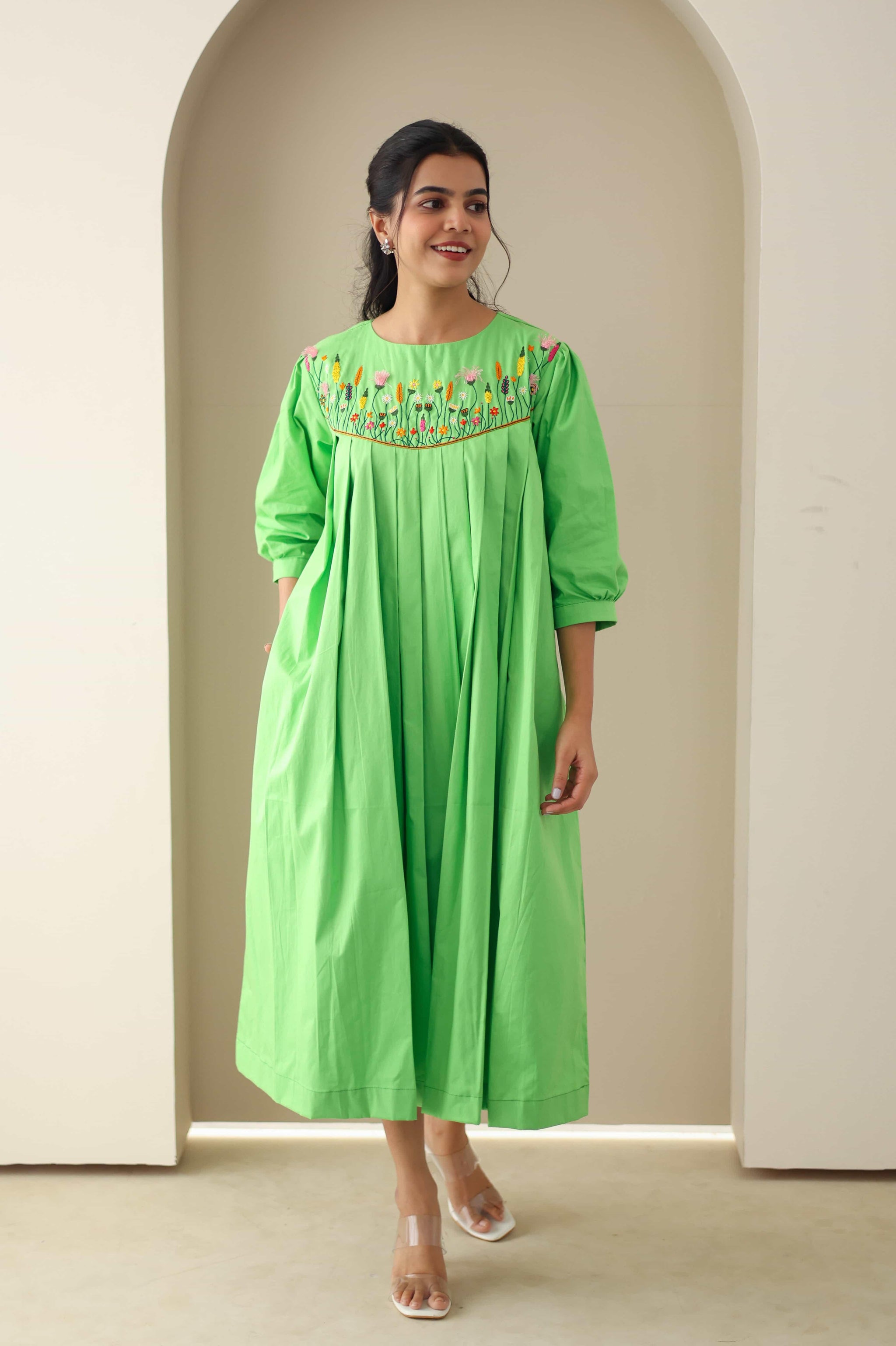 Woman wearing a green cotton poplin dress with floral embroidery and pleated front