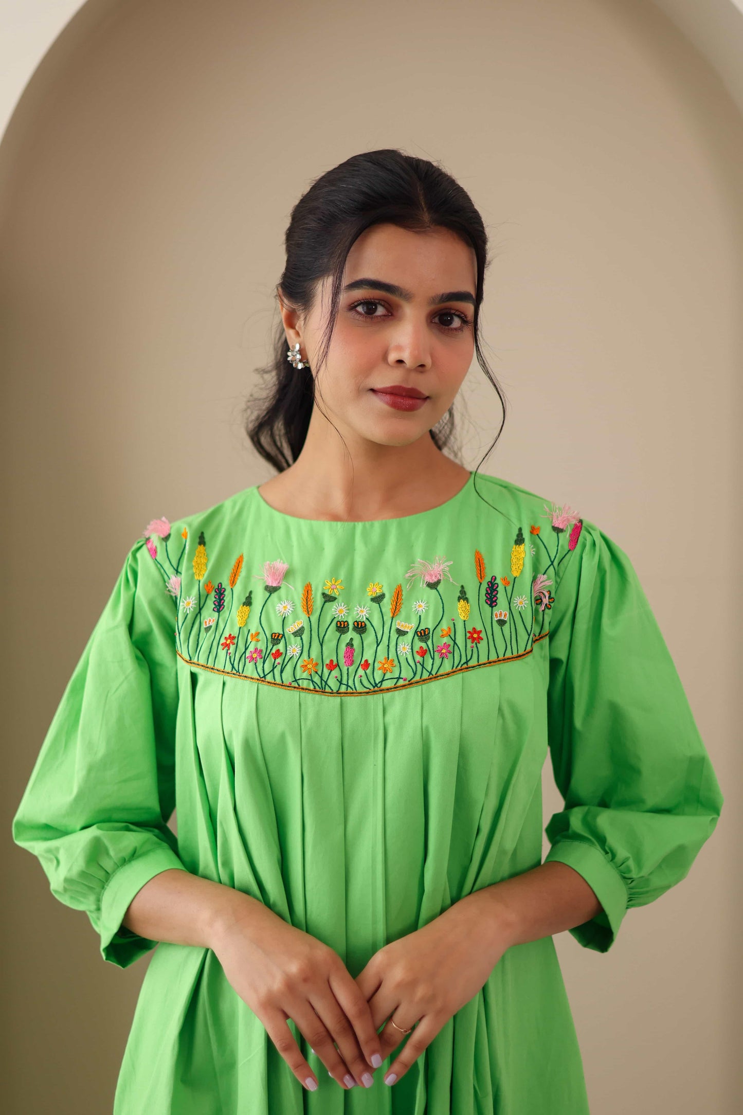 Woman wearing green cotton poplin dress with colorful floral embroidery and pleated front