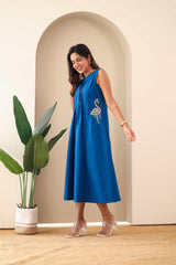 Woman wearing sleeveless navy blue embroidered cotton dress with flamingo motif, standing indoors.