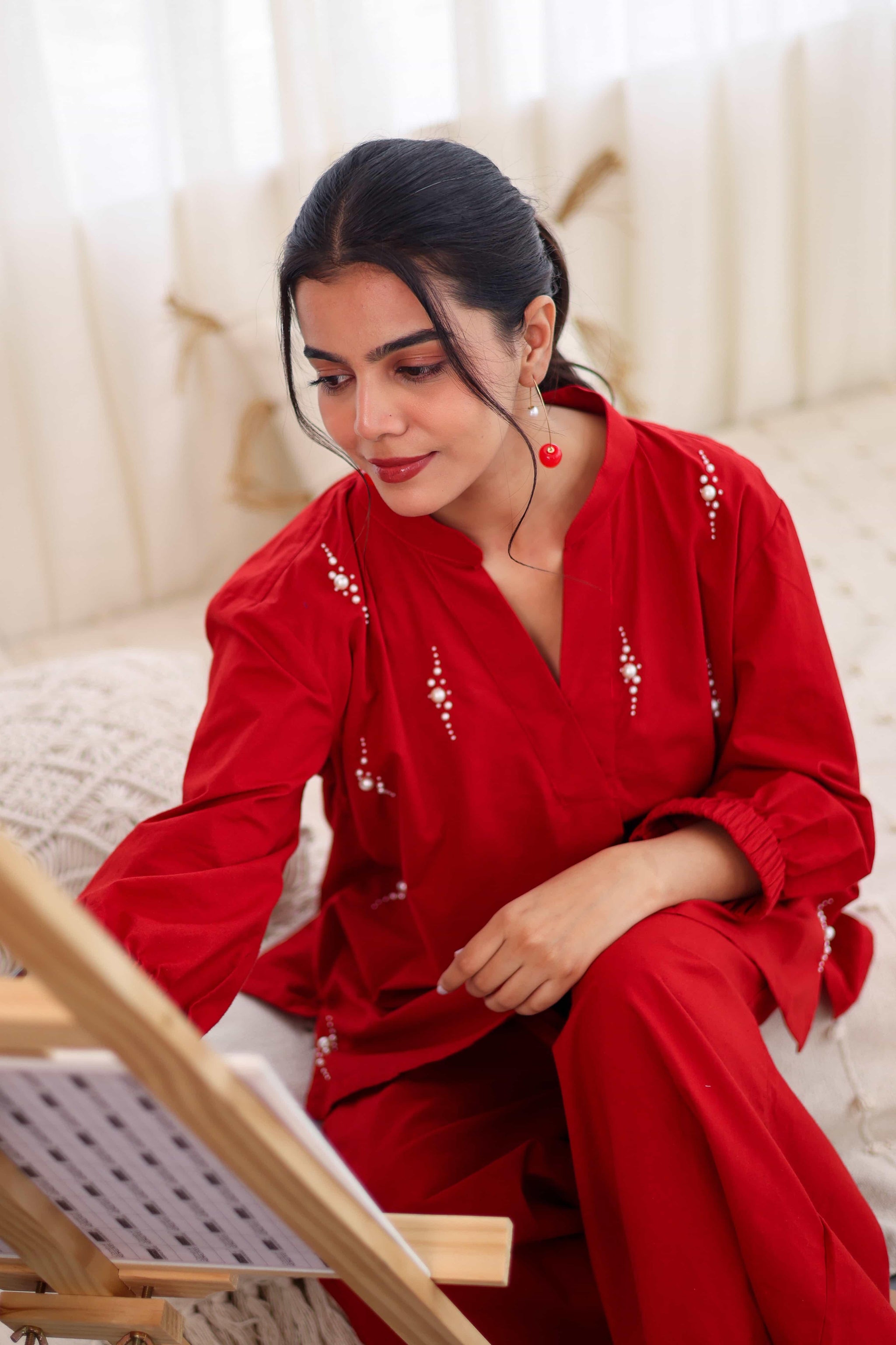 Woman in red pearl embroidered cotton co-ord set sitting indoors and painting